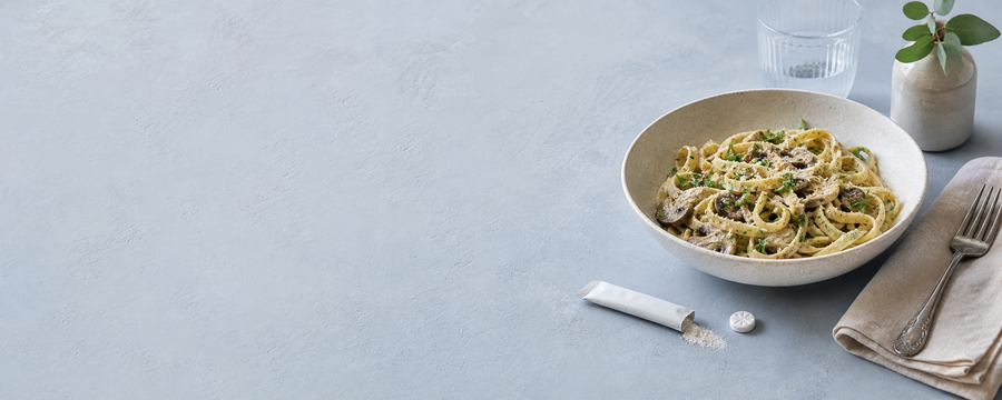 Pasta, a digestive enzyme powder packet, and a chewable mint arranged on a blue dining table